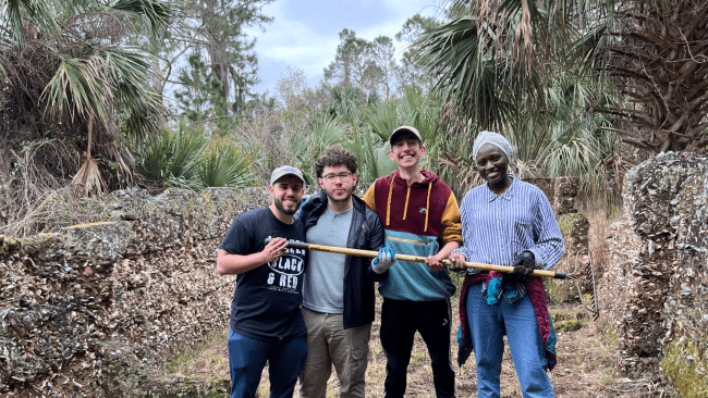 a group of four young people hold a wooden tool in a tropical scene