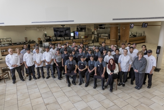 a group of chefs and dining staff pose together in the cafeteria