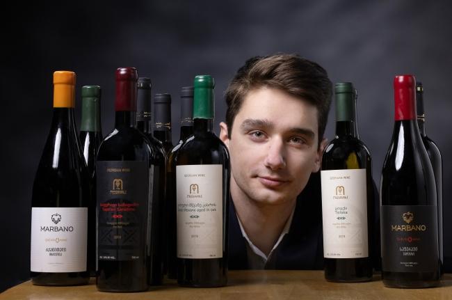a young white man behind a table covered with bottles of wine