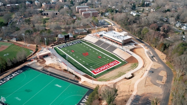 a large athletic stadium with a college campus in the distance, seen from above