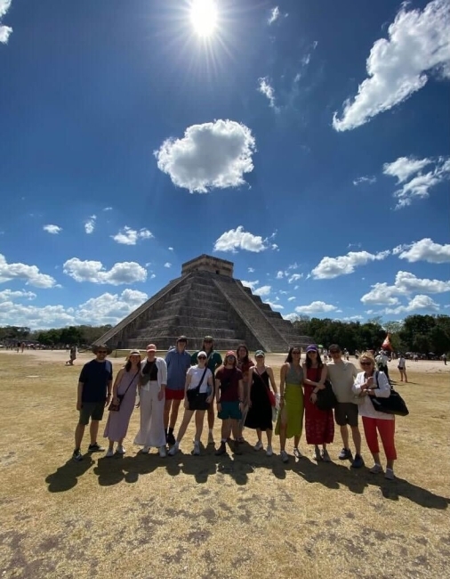 a group of students stand in front of ancient ruins on a sunny day