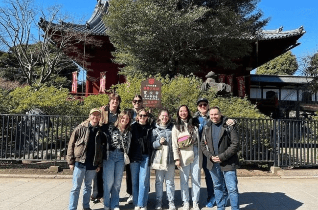 a group of students and their professor stand in front of a Japanese structure