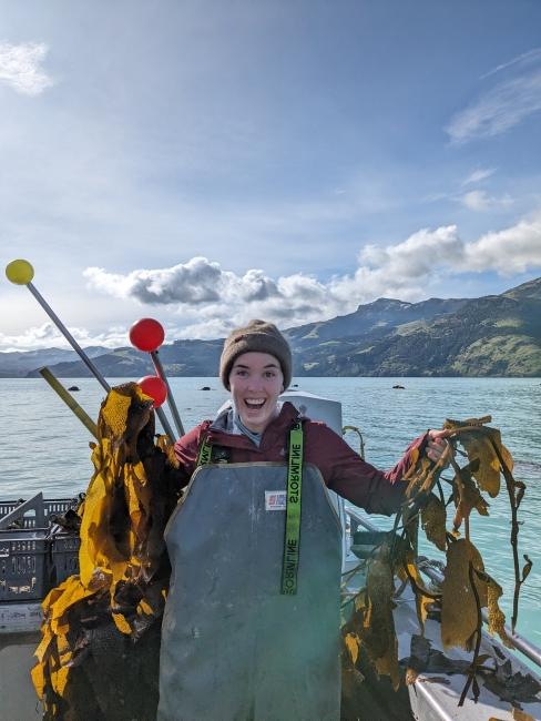 a young white woman smiling holding seaweed on a boat