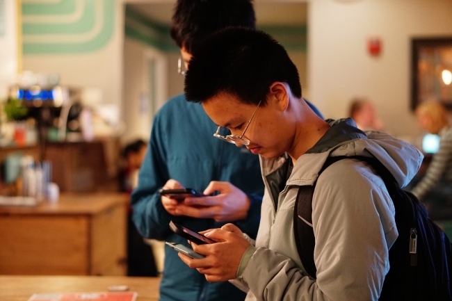 two young men stand in a coffee shop on their phones