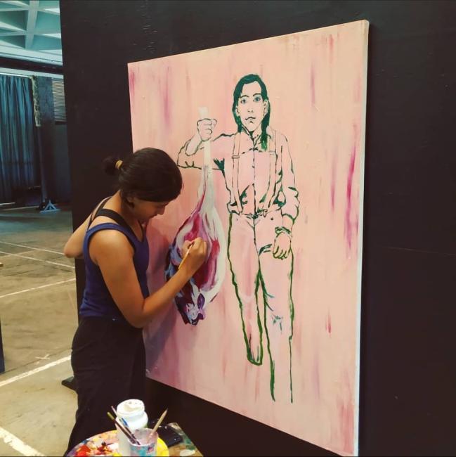 a young woman stands in front of a canvas working