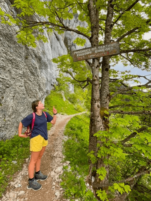 a young woman in hiking boots points at a trail marker on a mountain