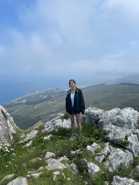 a young woman wearing hiking gear stands on a mountain top