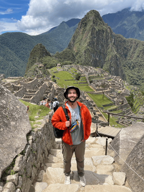 a young man stands on steps overlooking mountains in Peru
