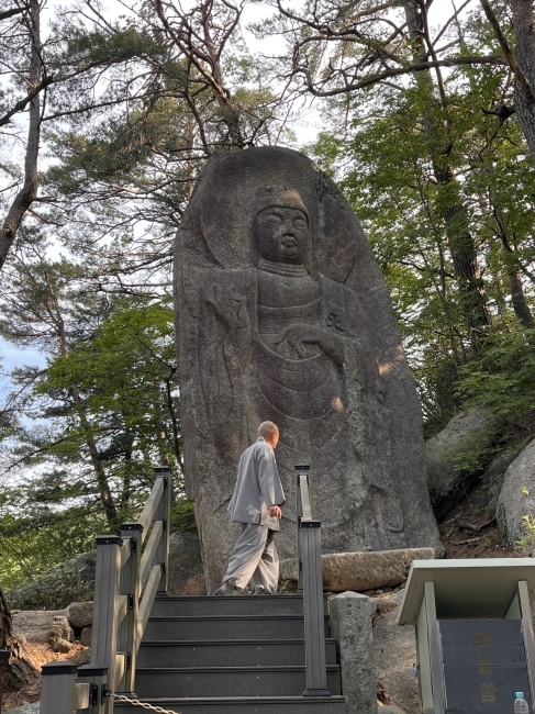 an older man walks in front of a Buddha statue