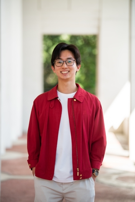 a young Asian man wearing a white t-shirt and red top with glasses