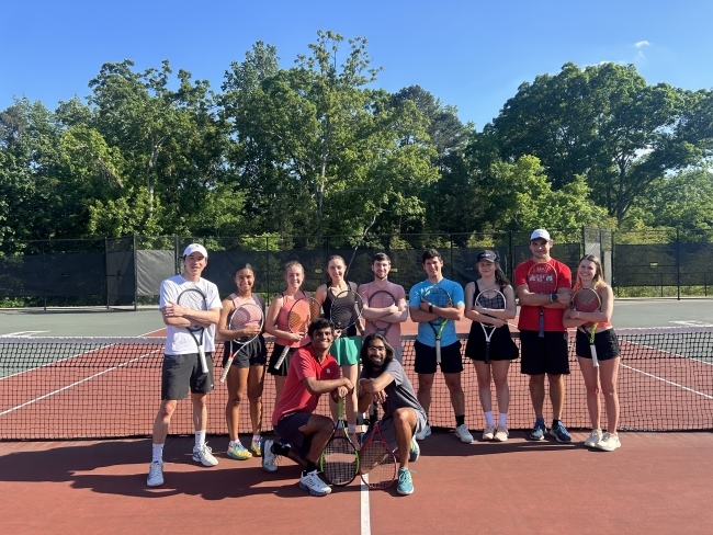 a group of students with tennis rackets on a court smiling