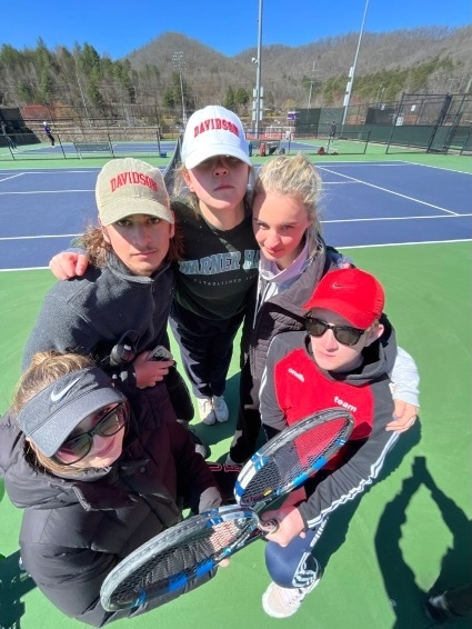 a group of young women standing together with tennis rackets on a court