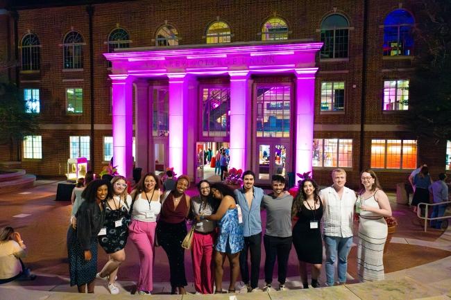 Young alums with arms around each other in front of a purple illuminated union