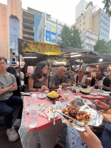 a group of people sit around a table of food on a street in Korea