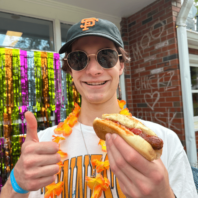 a young white man smiling holding a hot dog