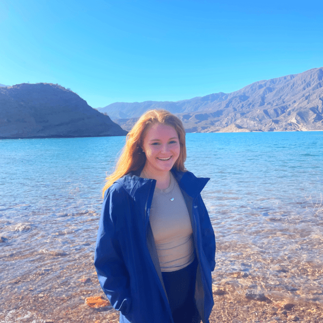 a young white woman standing in front of a lake