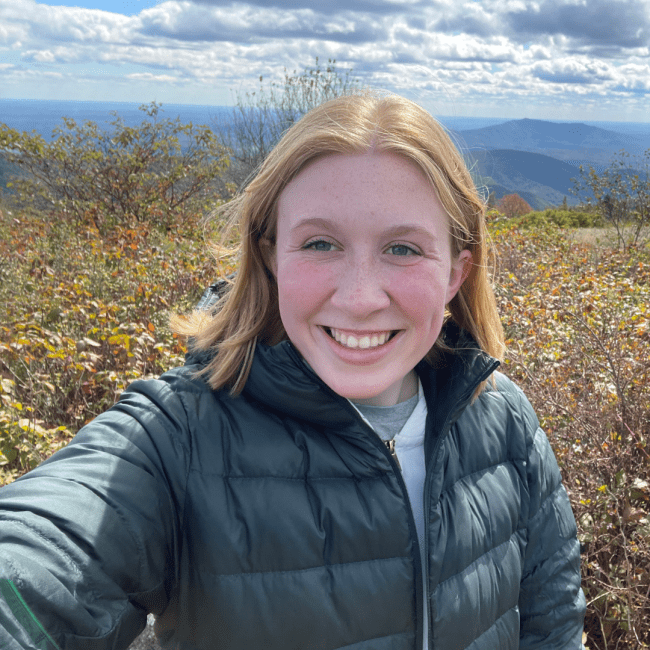 a young white woman in a jacket overlooking mountains