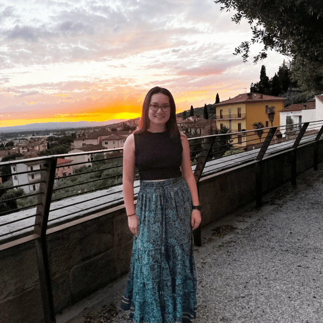 a young white woman standing in front of a sunset