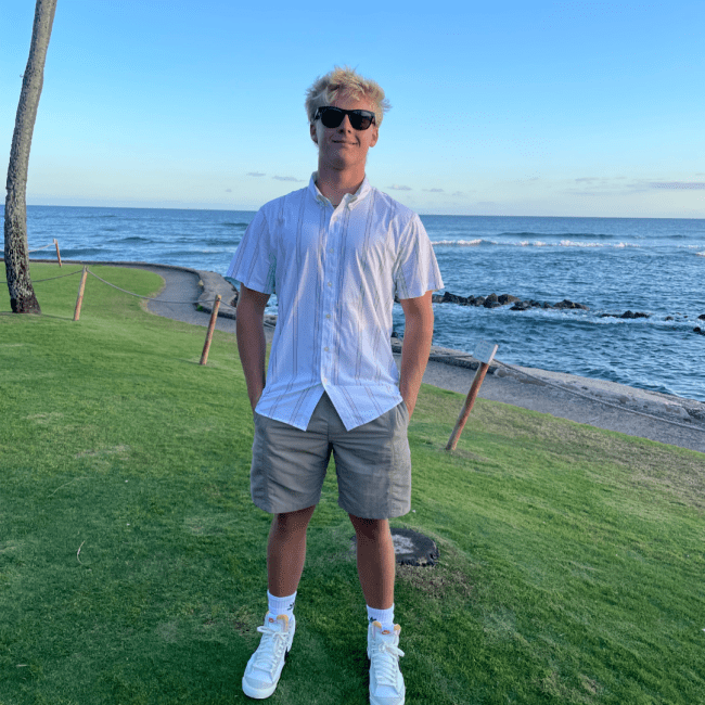 a young white man wearing a white top standing in front of the ocean