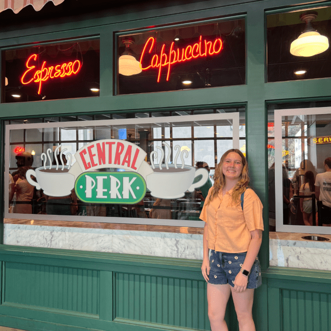 a young white woman standing in front of a coffee shop 