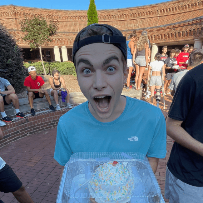 a young white man holding a cake and smiling big