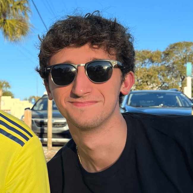 a young man wearing a black shirt and sunglasses on a sunny day