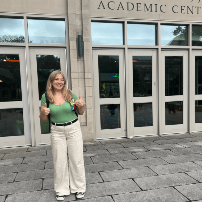 a young white woman wearing a green top and trousers in front of an academic building