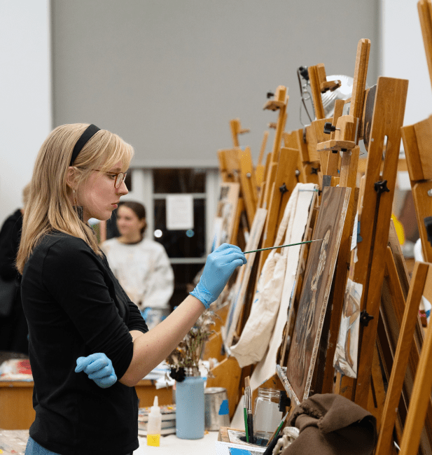 a young woman paints on a canvas in a studio