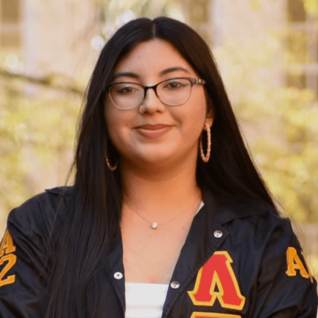 a young Latina woman smiling wearing glasses and a jacket