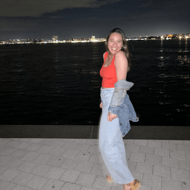 a young woman wearing a tank and jeans standing in front of a city skyline