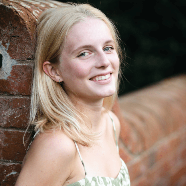 a young white woman leaning against a brick wall