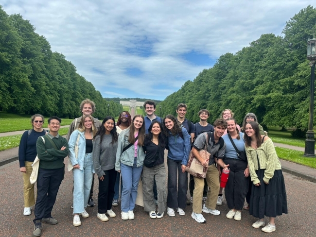 a group of students standing together surrounded by green trees and lawns