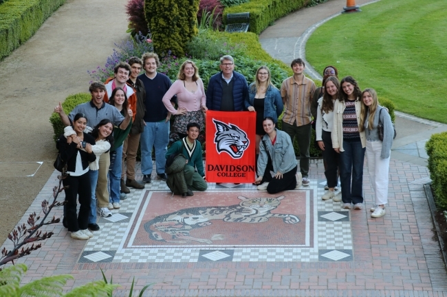 a group of students and some older people at an old castle holding a "Davidson College" banner