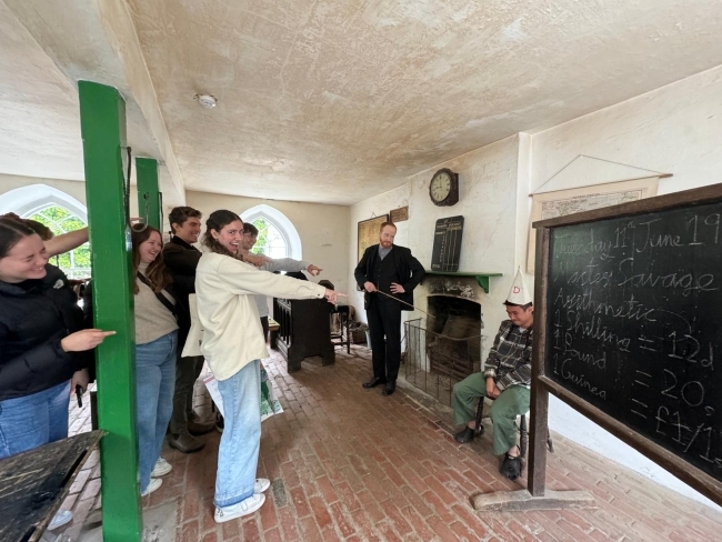 a group of students in an old classroom pointing in a funny way at a student