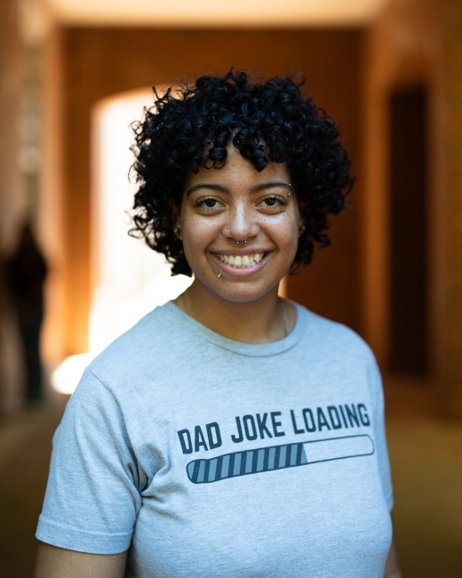 a young woman with dark curly black hair wearing a t-shirt and smiling