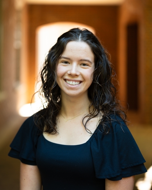 a young white woman with dark brown hair wearing a dark top and smiling