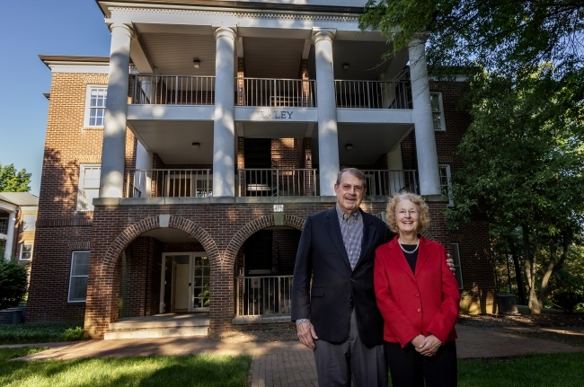 an older couple stands in front of a college residence hall