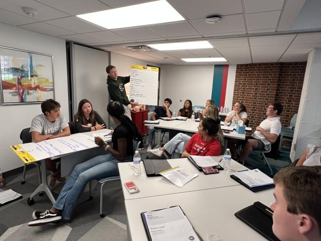 a group of students in a classroom looking at a man teaching