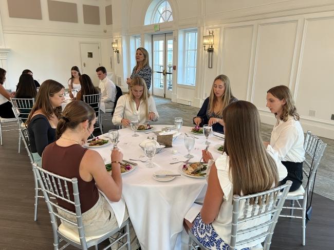 a group of students sit around a dining table talking and eating