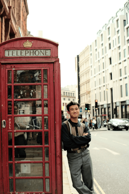 a young man stands next to a British telephone booth