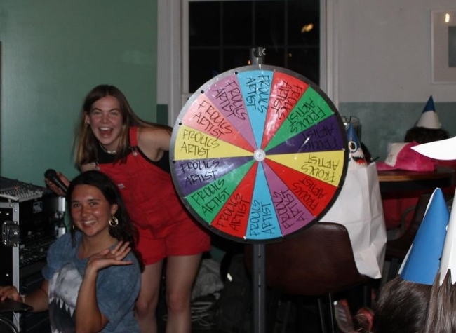 two young women stand next to a colorful wheel