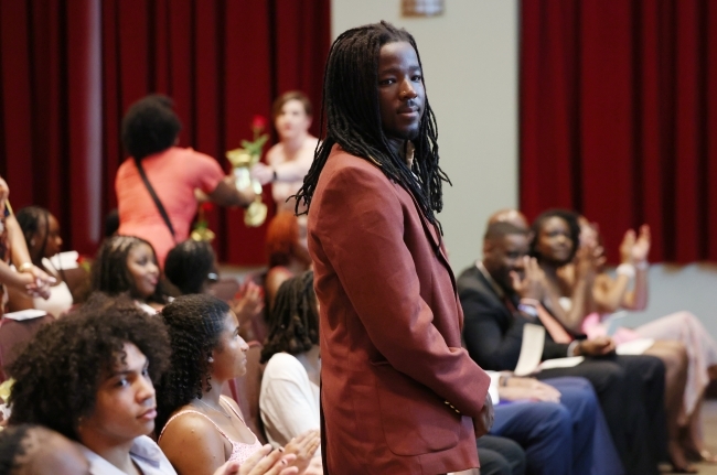 a young Black man in a suit smiles over a crowd