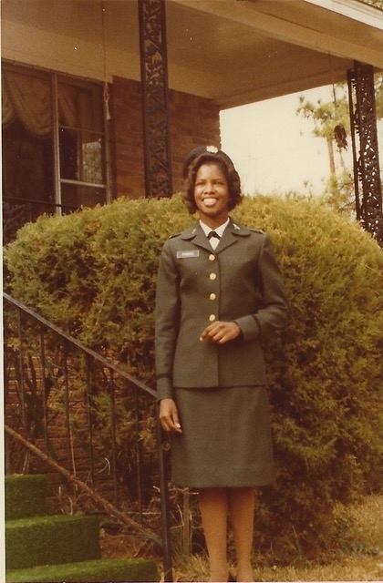 a young Black woman in military uniform standing outside a house