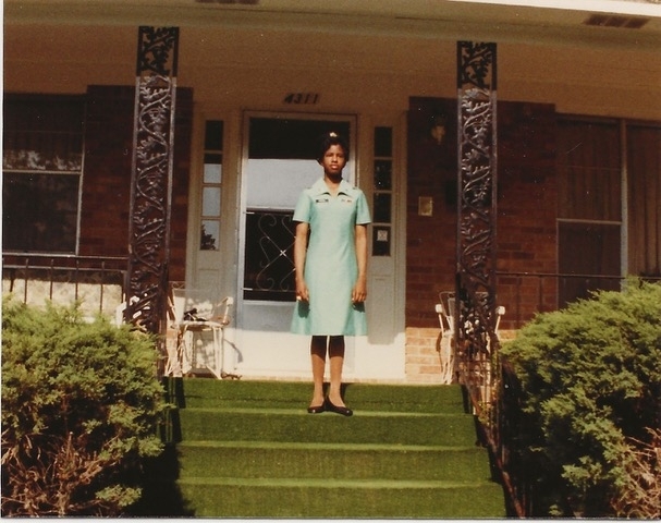 a young Black woman in uniform on the porch of a house