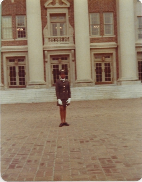 a young Black woman in uniform in front of a brick columned building