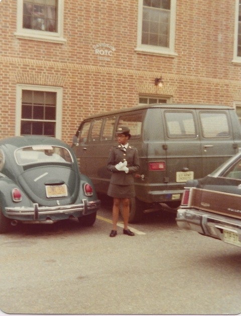 a young Black woman stands in front of a brick building that reads "ROTC"