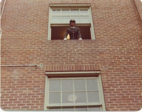 a young Black woman leans out a window