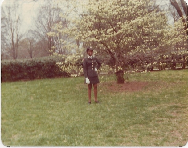 a young Black woman in uniform in front of a cherry blossom tree