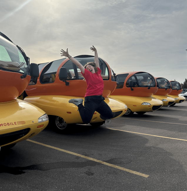 Emily Schmidtt '23 jumps in front of lined-up Weinermobiles