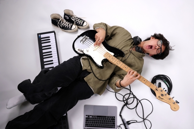 a young man wearing glasses laying on the ground playing the guitar